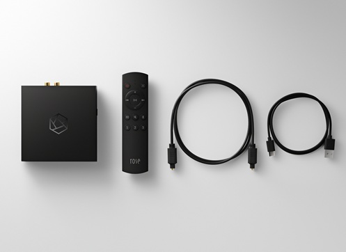 Black streaming media player with a geometric logo, accompanied by a remote and two cables (HDMI and power) arranged on a white surface.